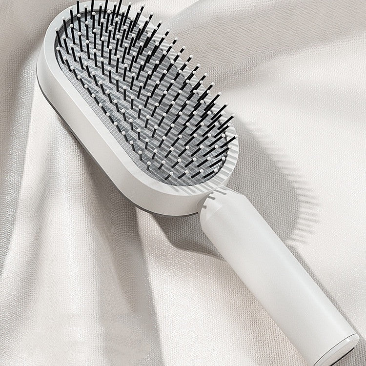 Weiße selbstreinigende Haarbürste mit flexiblen Borsten, stilvoll platziert auf einem glänzenden Stoff – modernes Beauty-Gadget für sanftes Entwirren, tägliche Haarpflege und glattes Styling