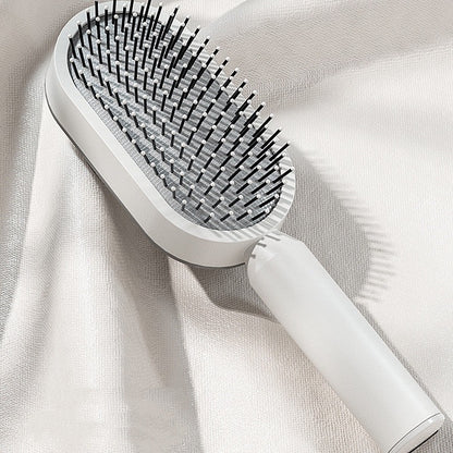 Weiße selbstreinigende Haarbürste mit flexiblen Borsten, stilvoll platziert auf einem glänzenden Stoff – modernes Beauty-Gadget für sanftes Entwirren, tägliche Haarpflege und glattes Styling